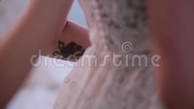 伴娘帮着穿上婚纱，在后面扣扣子。 早上准备有纹身的年轻新娘。